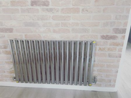 Horizontal chrome column radiator against an exposed brick wall