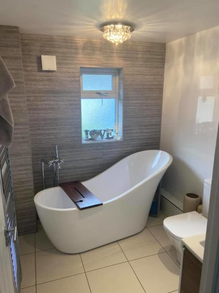Freestanding slipper bath with wooden bath caddy and woodgrain-effect feature wall
