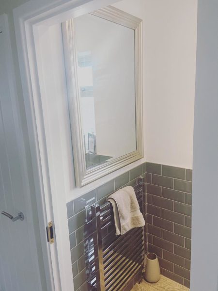 Framed bathroom mirror above grey metro tiling with a chrome heated towel rail